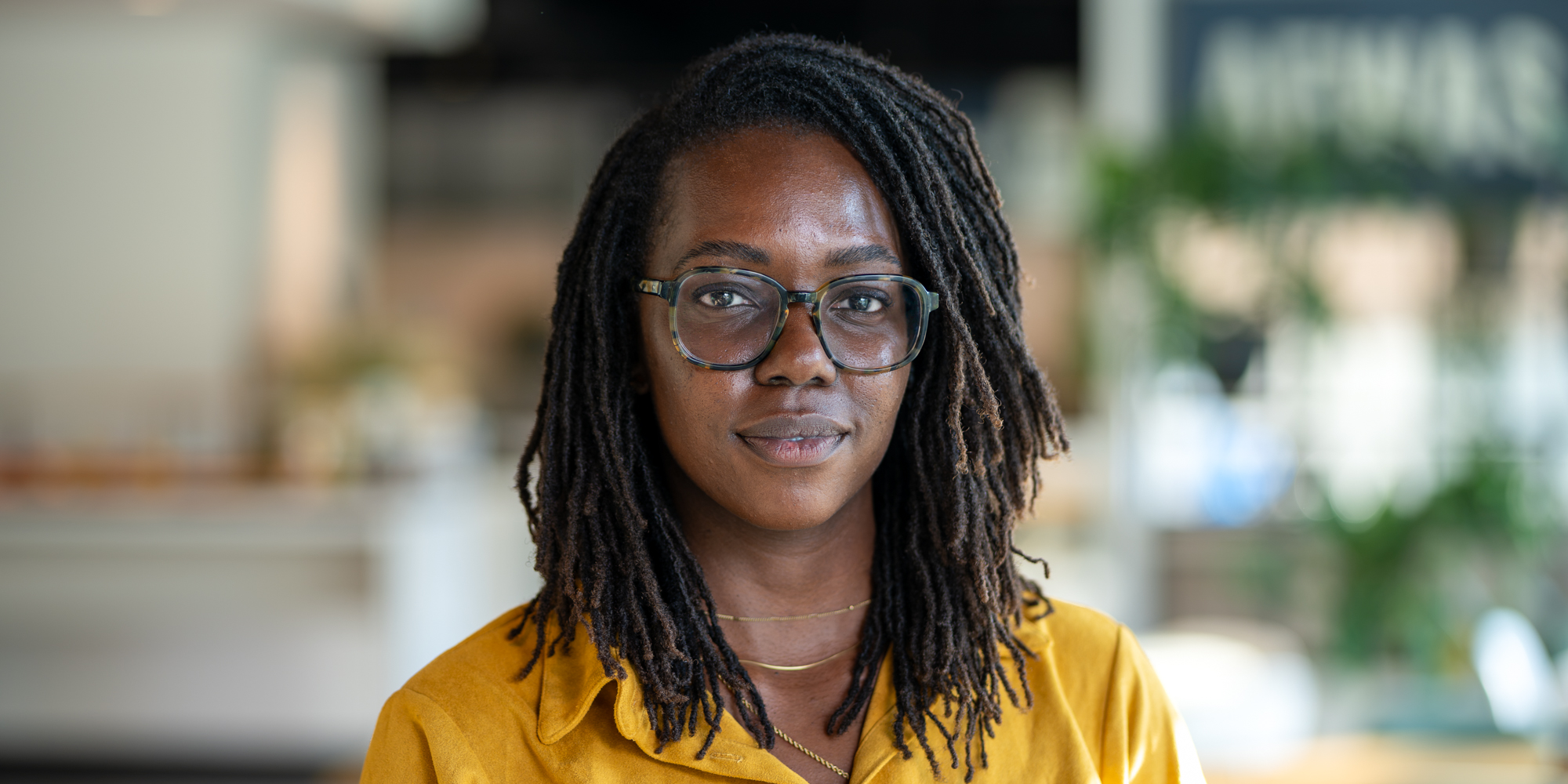 Zakelijk portret van een vrouw met bril en gele blouse, gefotografeerd op locatie.